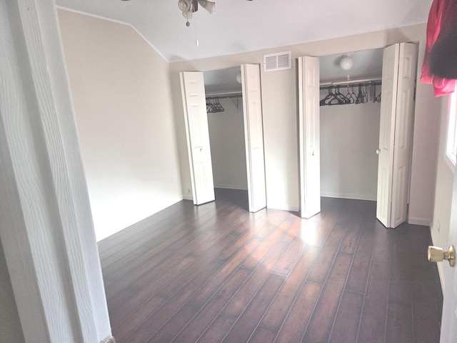 unfurnished bedroom featuring vaulted ceiling, baseboards, visible vents, two closets, and dark wood-type flooring