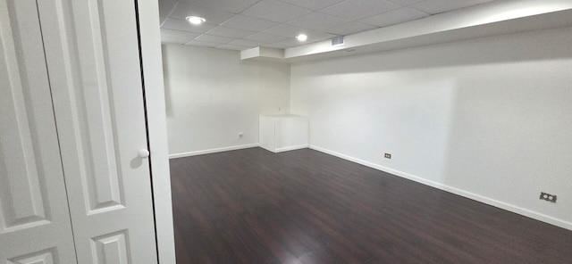interior space with baseboards, a drop ceiling, and dark wood finished floors