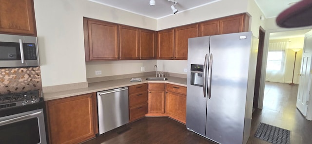 kitchen with light countertops, a sink, appliances with stainless steel finishes, brown cabinets, and dark wood-type flooring