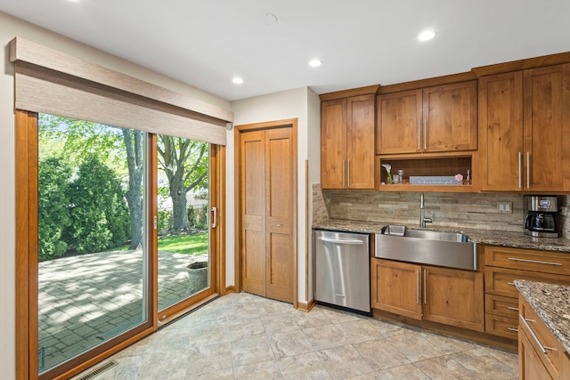 kitchen with dishwasher, a sink, backsplash, dark stone countertops, and brown cabinets
