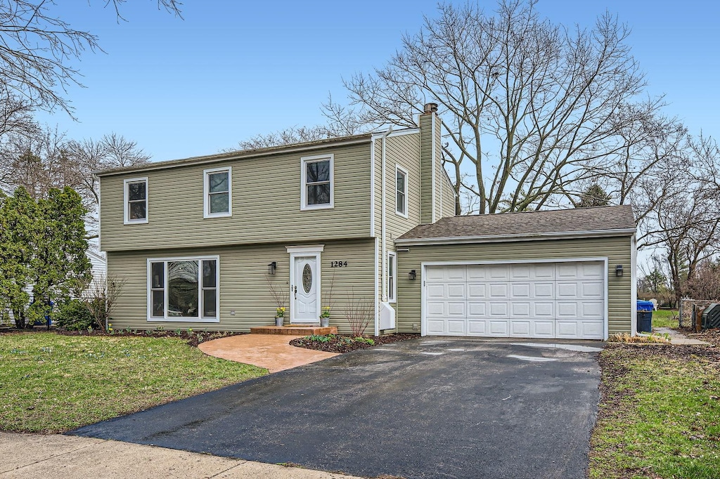 colonial inspired home with aphalt driveway, an attached garage, a chimney, and a front yard