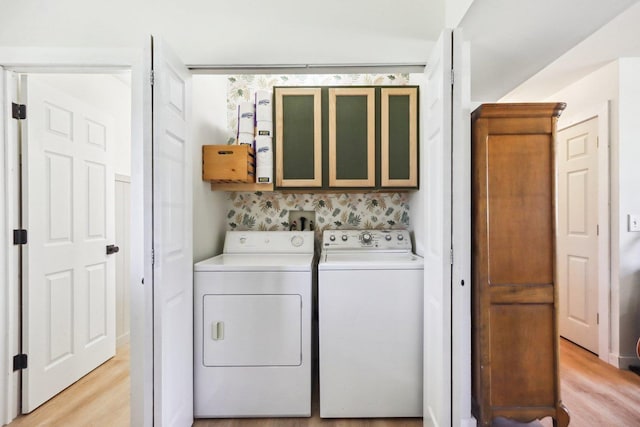 clothes washing area with light wood-style flooring, cabinet space, and washing machine and clothes dryer