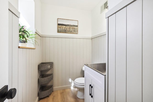 bathroom with visible vents, vanity, wood finished floors, toilet, and a wainscoted wall