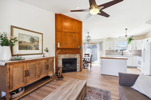 living area with a fireplace, ceiling fan, lofted ceiling, and light wood-style floors