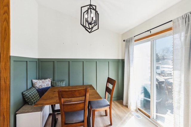 dining space with visible vents, light wood-type flooring, a decorative wall, and an inviting chandelier