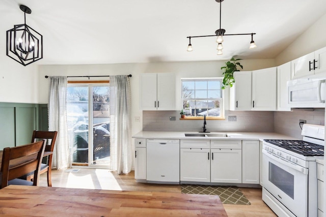 kitchen with a sink, light wood finished floors, white appliances, white cabinetry, and backsplash