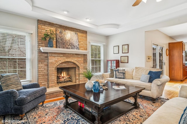 living room featuring a tray ceiling, a fireplace, wood finished floors, and a ceiling fan
