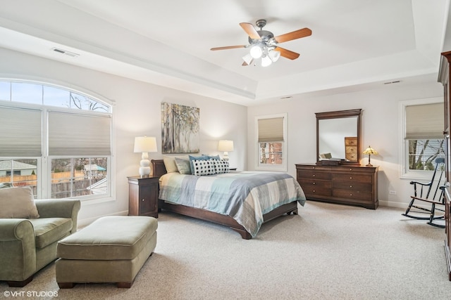 carpeted bedroom with a tray ceiling, baseboards, visible vents, and ceiling fan