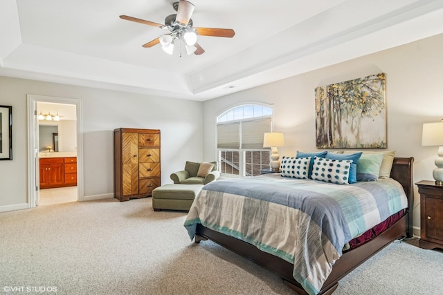 bedroom featuring connected bathroom, a tray ceiling, light carpet, baseboards, and ceiling fan