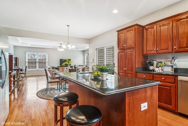 kitchen with open floor plan, a breakfast bar area, stainless steel dishwasher, a kitchen island, and light wood-style floors
