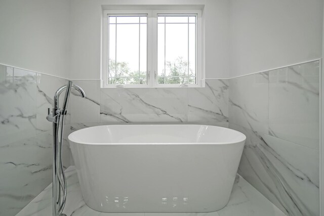 bathroom with marble finish floor, a freestanding tub, and wainscoting