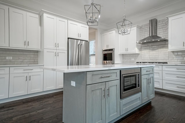 kitchen featuring crown molding, an inviting chandelier, a center island, wall chimney range hood, and appliances with stainless steel finishes