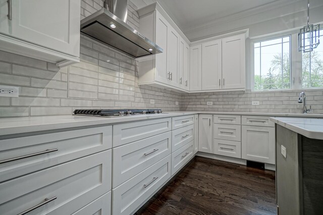 kitchen featuring a sink, tasteful backsplash, dark wood-style floors, wall chimney range hood, and white cabinets