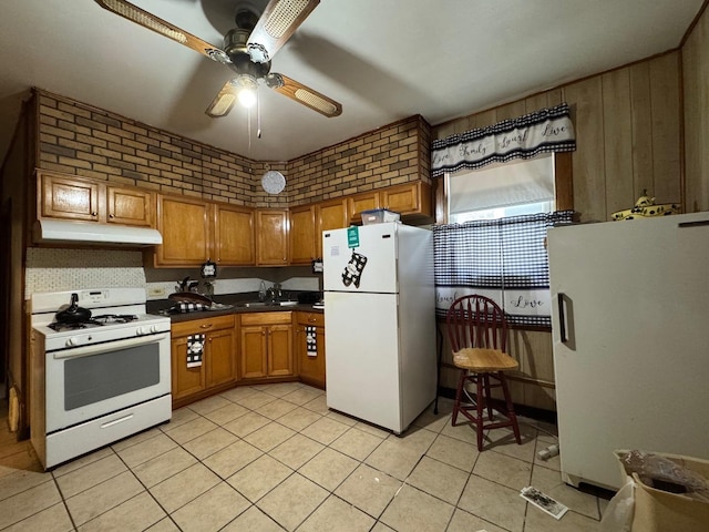 kitchen featuring white appliances, under cabinet range hood, brick wall, ceiling fan, and brown cabinetry