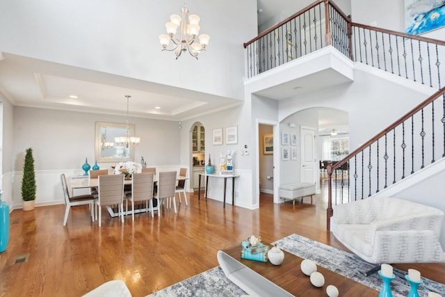 living area featuring a tray ceiling, arched walkways, a notable chandelier, and wood finished floors