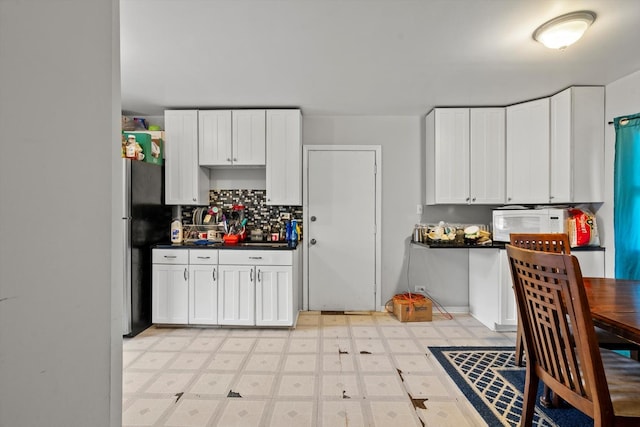 kitchen with white microwave, backsplash, dark countertops, freestanding refrigerator, and light floors