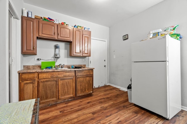 kitchen with dark wood-style floors, brown cabinets, light countertops, baseboards, and freestanding refrigerator