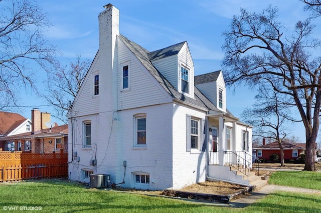 view of side of home with a chimney, a lawn, brick siding, central AC, and fence