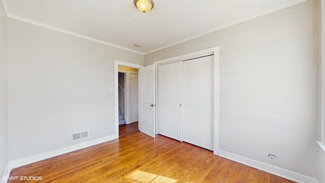 unfurnished bedroom with visible vents, ornamental molding, a closet, baseboards, and light wood-style flooring