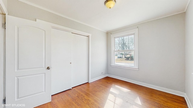 unfurnished bedroom with crown molding, baseboards, a closet, and light wood finished floors