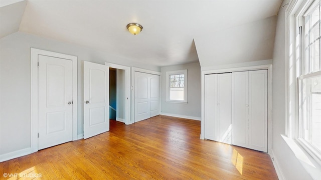 unfurnished bedroom featuring vaulted ceiling, baseboards, two closets, and light wood finished floors