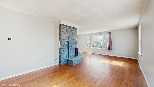 unfurnished living room with baseboards, wood finished floors, visible vents, and a stone fireplace