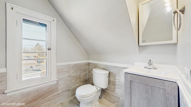 half bath with vanity, lofted ceiling, toilet, tile walls, and a wainscoted wall