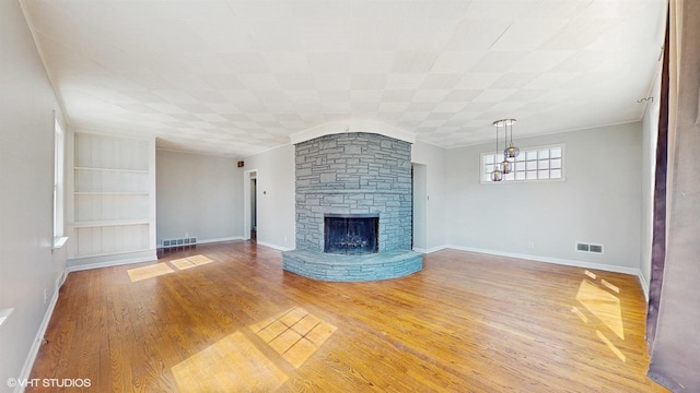 unfurnished living room featuring light wood finished floors, a stone fireplace, built in features, baseboards, and visible vents