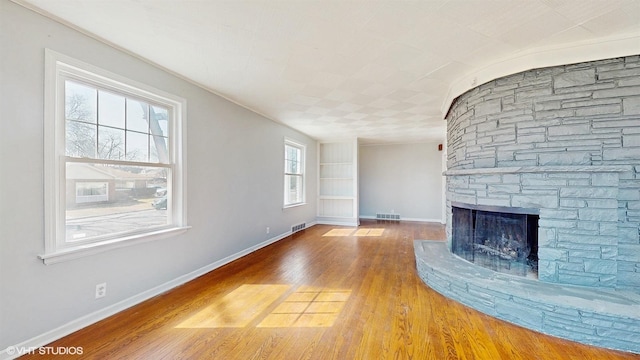unfurnished living room with baseboards, a fireplace, wood finished floors, and visible vents