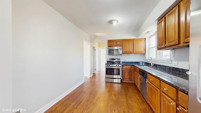 kitchen featuring brown cabinets, a sink, dark stone countertops, dark wood-style floors, and stainless steel appliances