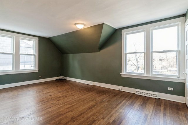 additional living space featuring dark wood-type flooring, lofted ceiling, visible vents, and baseboards