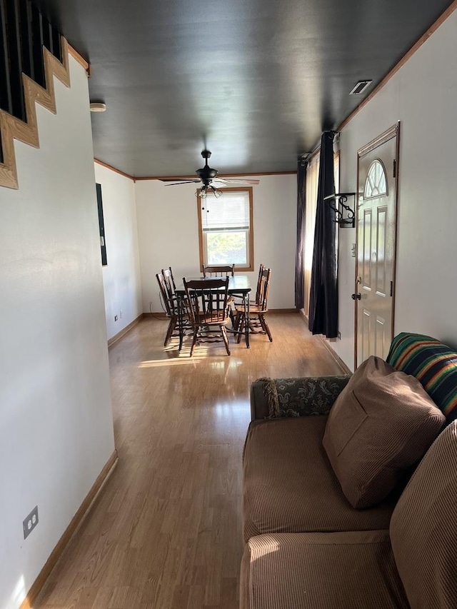 living area with ornamental molding, ceiling fan, baseboards, and light wood-style floors