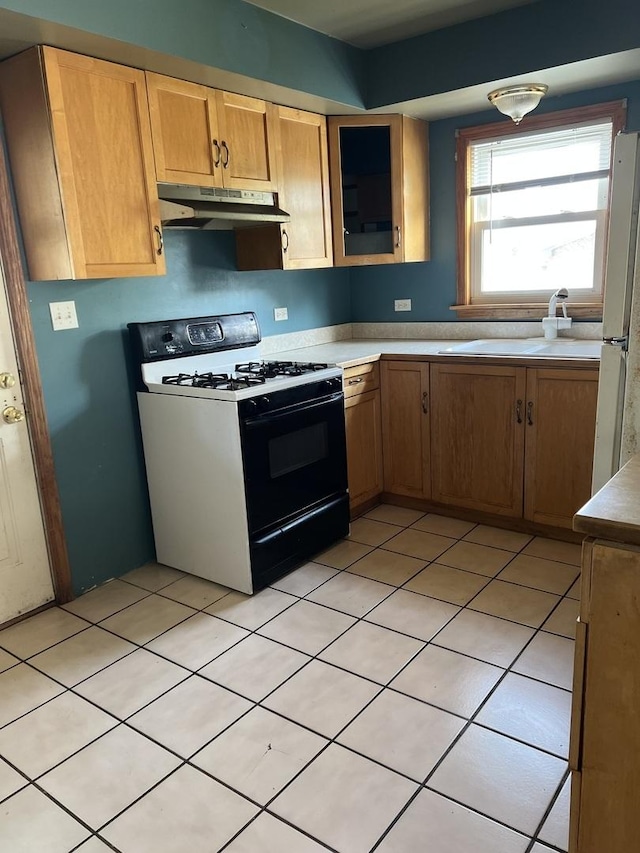 kitchen with a sink, under cabinet range hood, light countertops, gas stove, and freestanding refrigerator