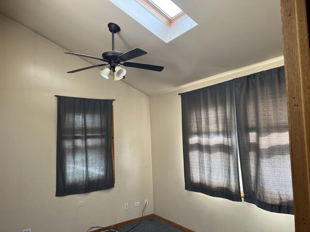carpeted empty room featuring lofted ceiling with skylight, ceiling fan, and baseboards