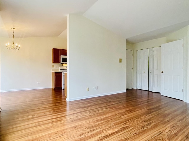 unfurnished living room featuring baseboards, an inviting chandelier, vaulted ceiling, and light wood-style flooring
