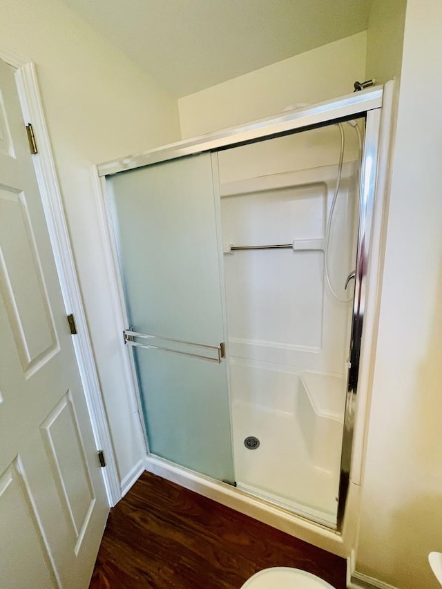bathroom with baseboards, wood finished floors, and a shower stall