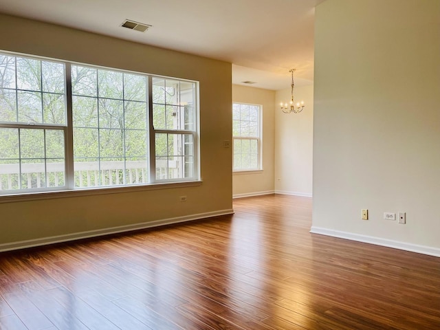 empty room with baseboards, visible vents, a chandelier, and dark wood-style floors