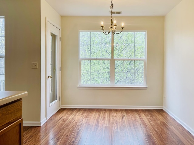 unfurnished dining area with baseboards, wood finished floors, visible vents, and a notable chandelier