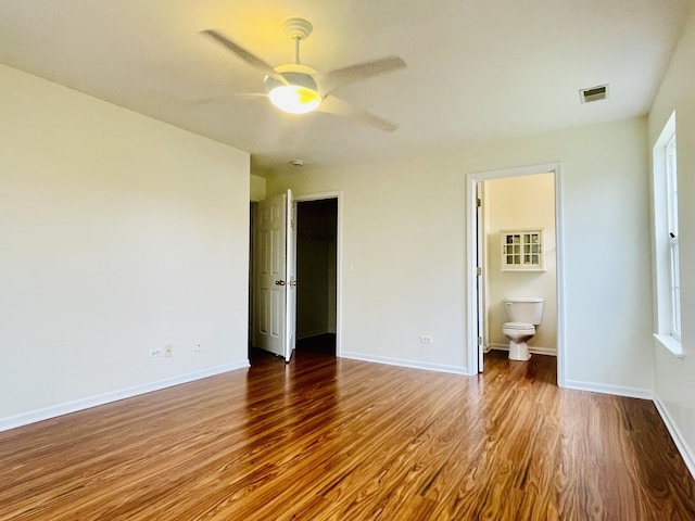 unfurnished bedroom featuring wood finished floors, ensuite bathroom, ceiling fan, baseboards, and visible vents