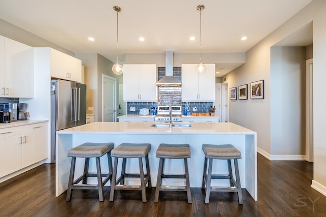 kitchen with wall chimney range hood, an island with sink, a kitchen breakfast bar, and stainless steel appliances
