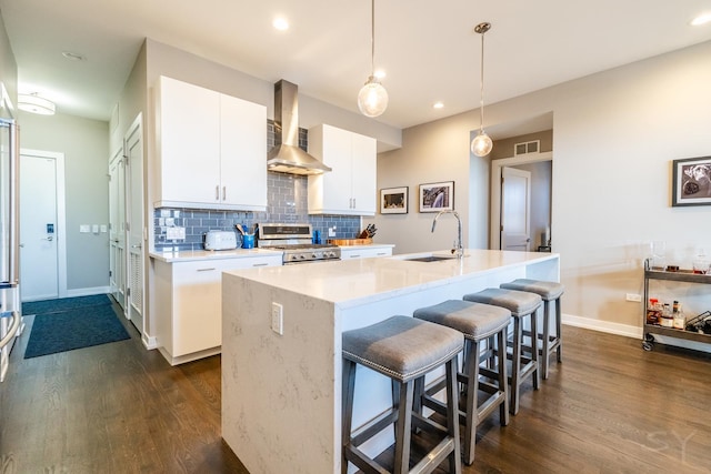 kitchen featuring stainless steel gas stove, dark wood-type flooring, wall chimney range hood, a sink, and backsplash