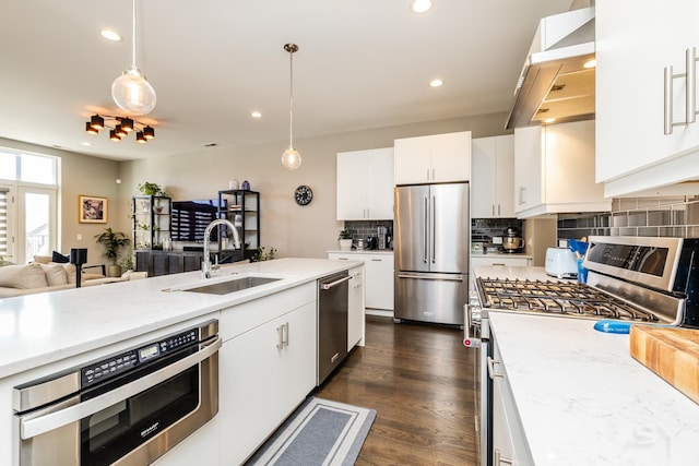 kitchen with range hood, a sink, open floor plan, appliances with stainless steel finishes, and backsplash