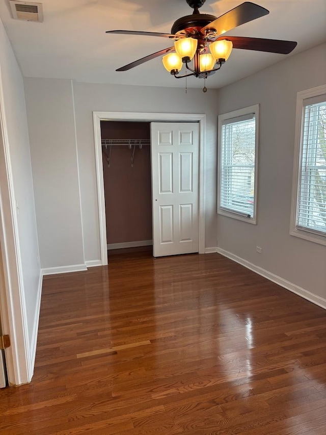 unfurnished bedroom with a closet, visible vents, baseboards, ceiling fan, and wood finished floors