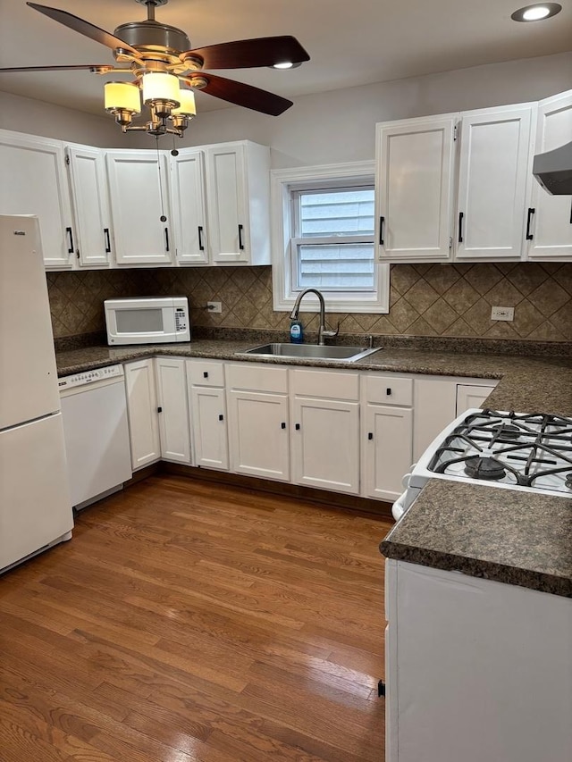 kitchen featuring dark wood-style flooring, a sink, dark countertops, and white appliances