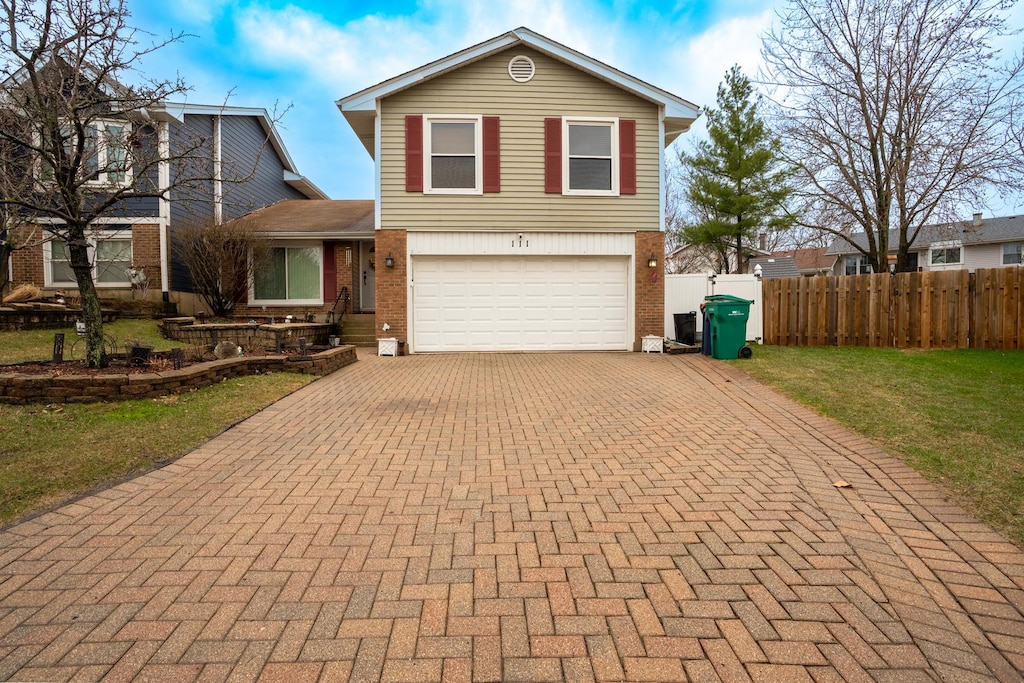 traditional-style house with a garage, fence, brick siding, a front lawn, and decorative driveway