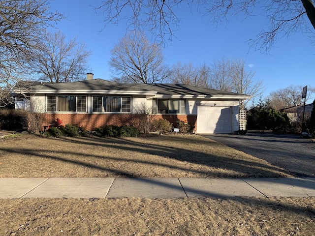 ranch-style home with driveway, a chimney, a front yard, a garage, and brick siding