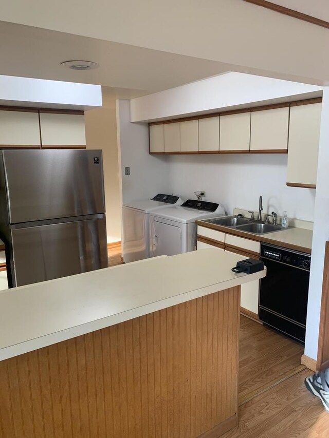 kitchen with a sink, white cabinets, freestanding refrigerator, black dishwasher, and washer and dryer