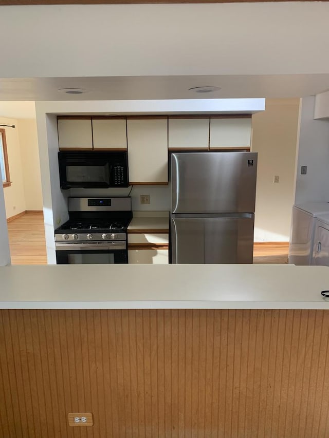 kitchen with light countertops, washer / clothes dryer, stainless steel appliances, and wood finished floors