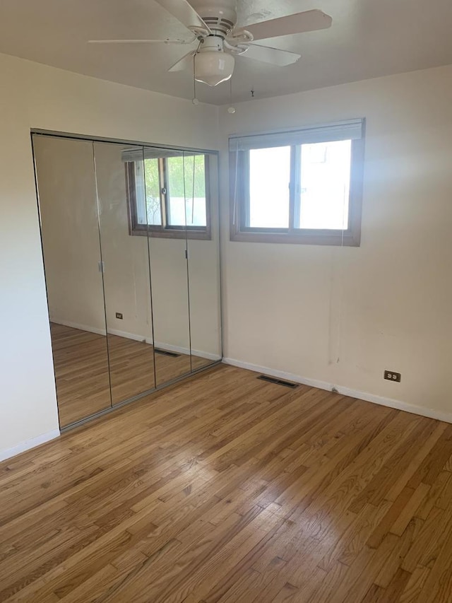 unfurnished bedroom with baseboards, a closet, wood finished floors, and multiple windows