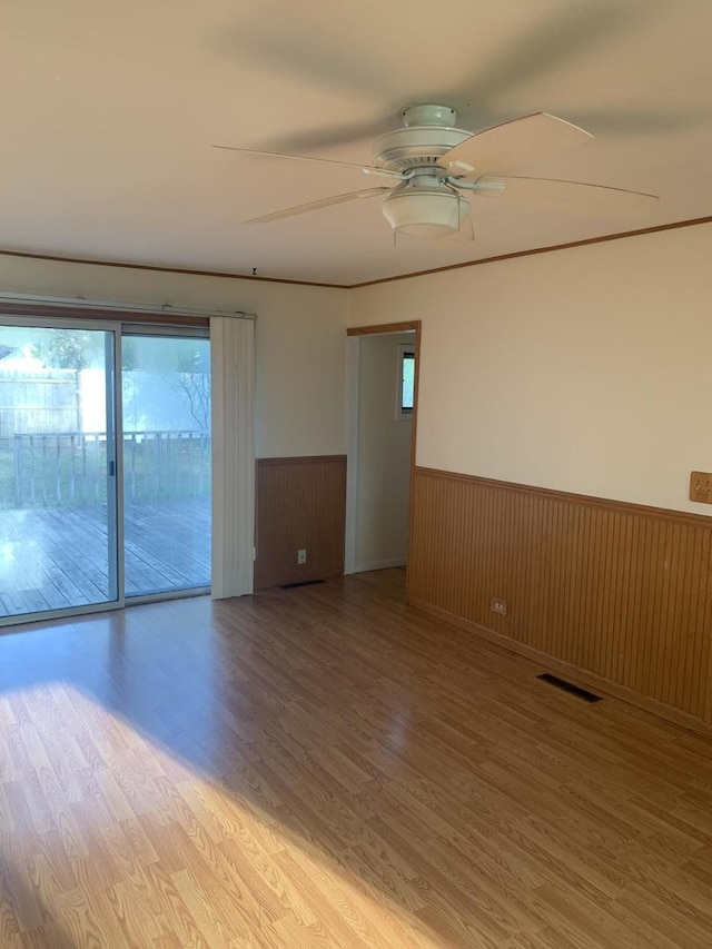 empty room featuring a wainscoted wall, plenty of natural light, light wood-type flooring, and visible vents